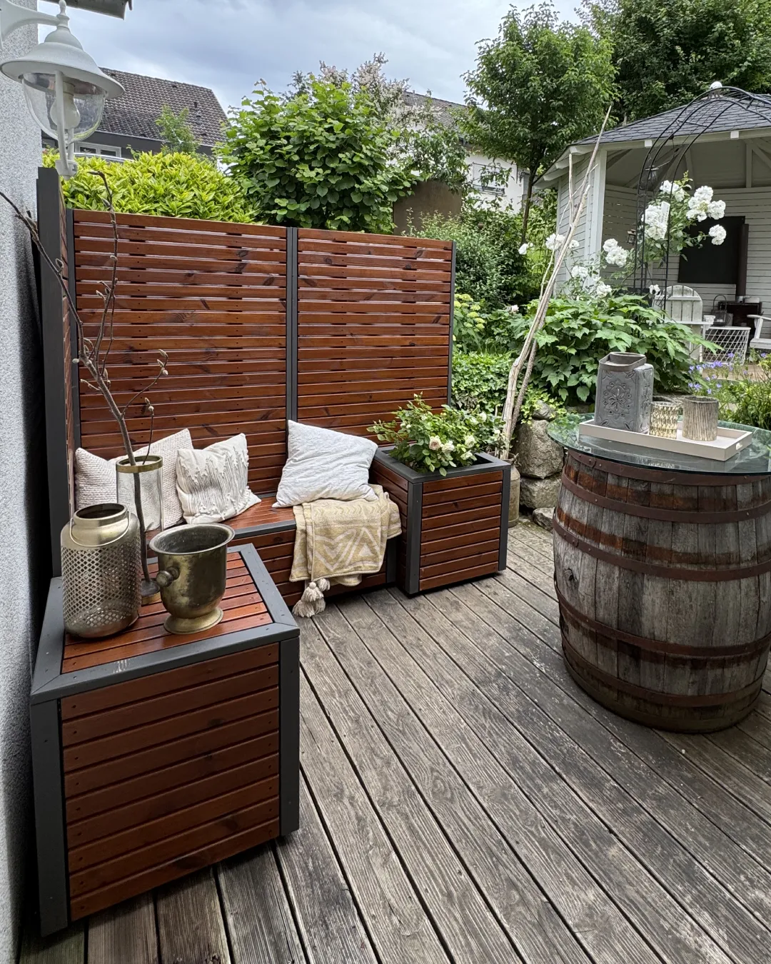 Geschützter Gartenraum mit Sichtschutz, Sitzbank, Pflanzkübel und Pavillon im Hintergrund